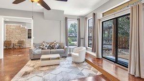 A spacious living room with a large window, a ceiling fan, and a stone accent wall.