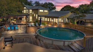 A pool area with a wooden deck, lounge chairs, and a barbecue grill.
