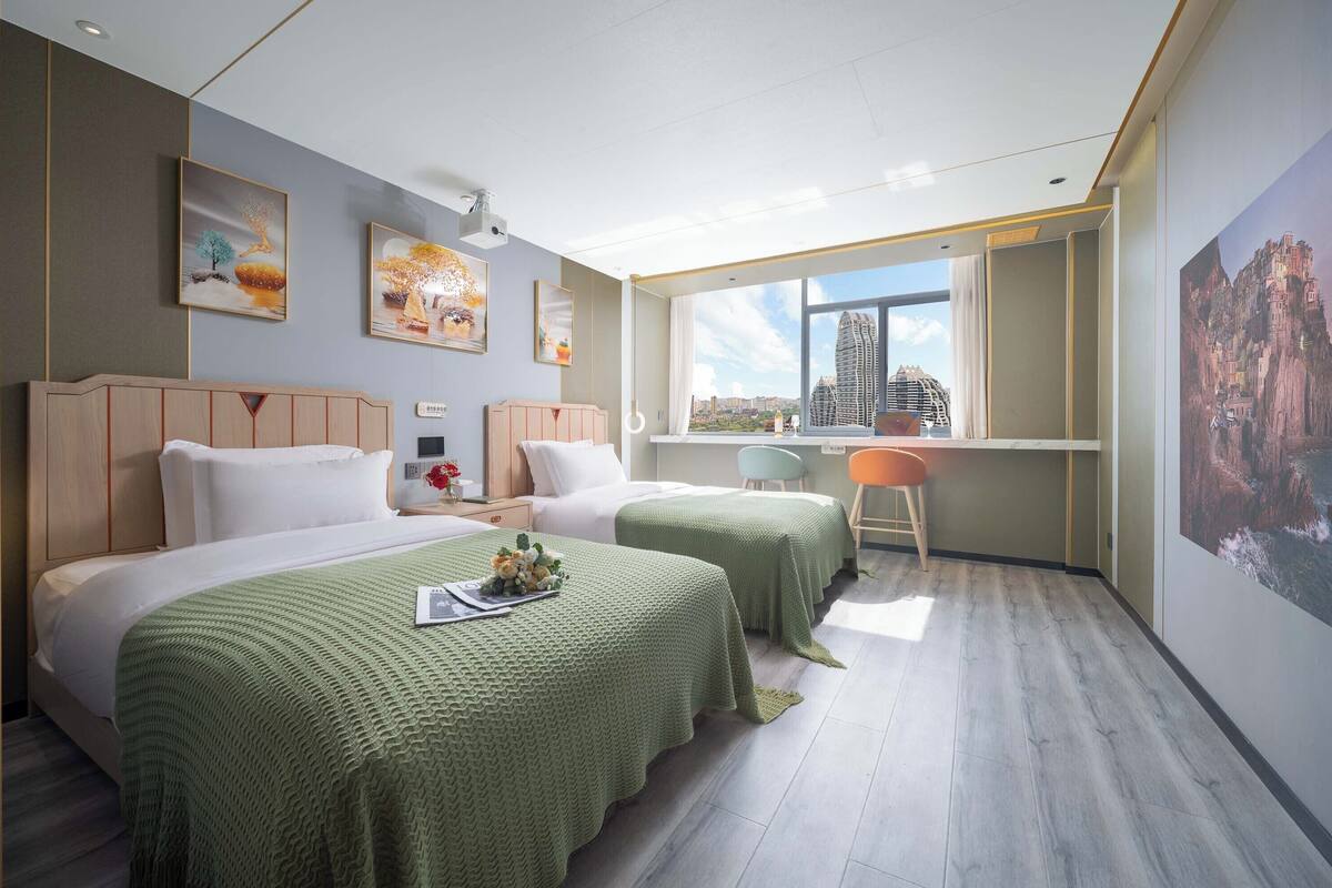 Hotellihuone, jossa on kaksi sänkyä, työpöytä ja suuri ikkuna, josta avautuu näkymä kaupunkiin.