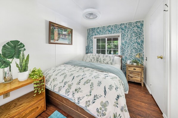 A bedroom with a bed, a bedside table, a nightstand, a window, and a wall with a leafy pattern. - 2 Lake Cabins Pool+hottub Game Room 23acs (Highland Lake)