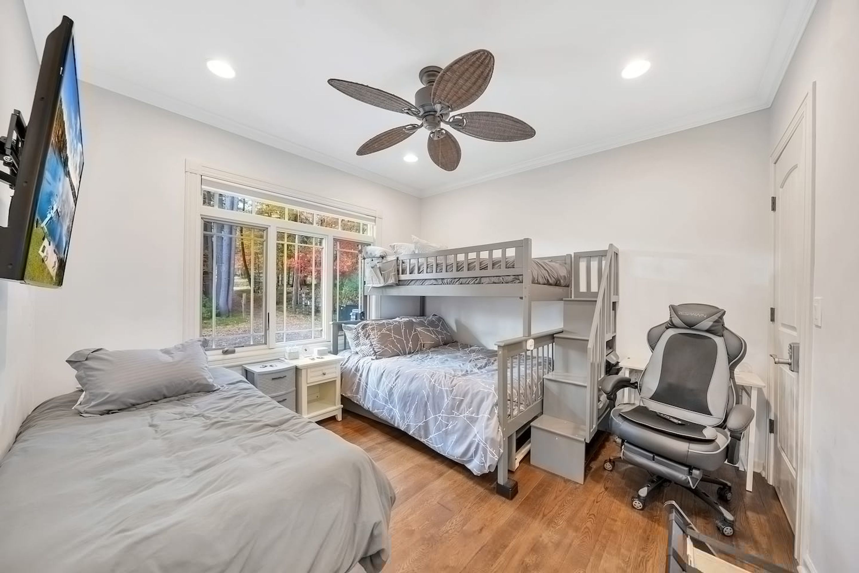Une chambre avec un lit superposé, un bureau, un fauteuil de jeu et un ventilateur de plafond.