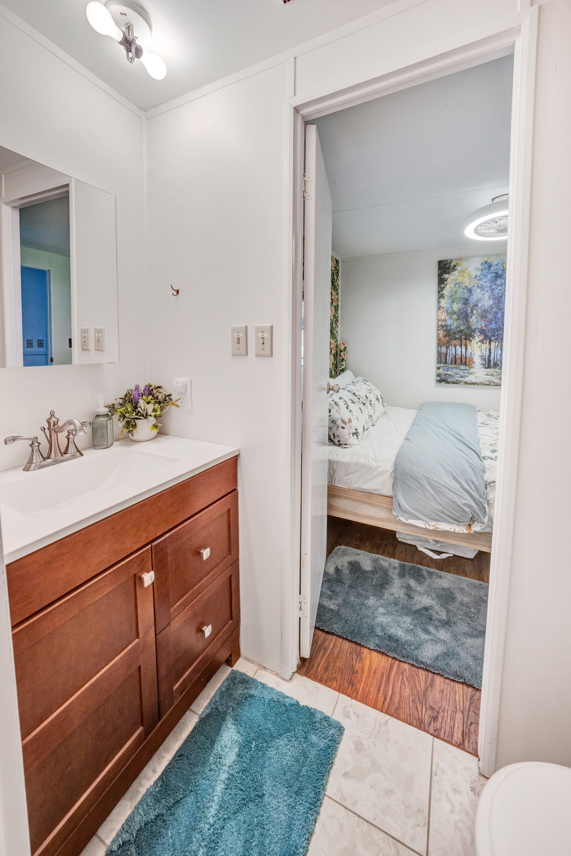 A bathroom with a white sink, wooden vanity, and a blue rug.
