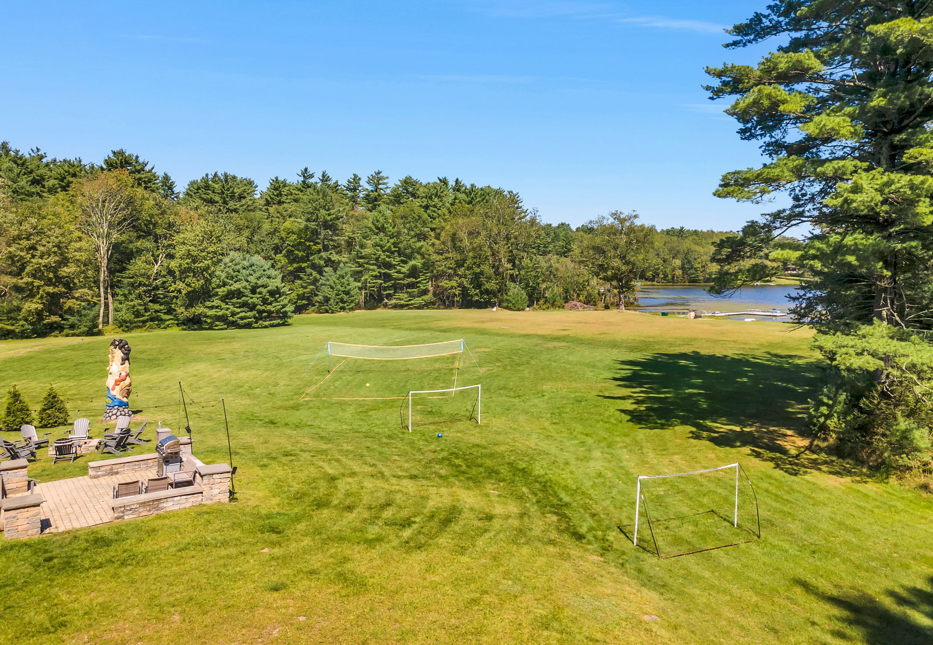 A well-maintained grassy area with a soccer goal, a barbecue setup, and a lake in the background.