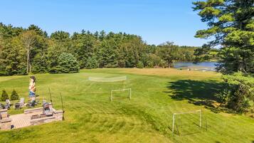 A well-maintained grassy area with a soccer goal, a barbecue setup, and a lake in the background.