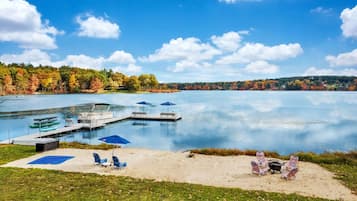 A lakeside view with a dock, boats, and beach chairs.