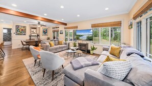 A spacious living room with a fireplace, comfortable seating, a dining area, and large windows offering a view of the outdoors.