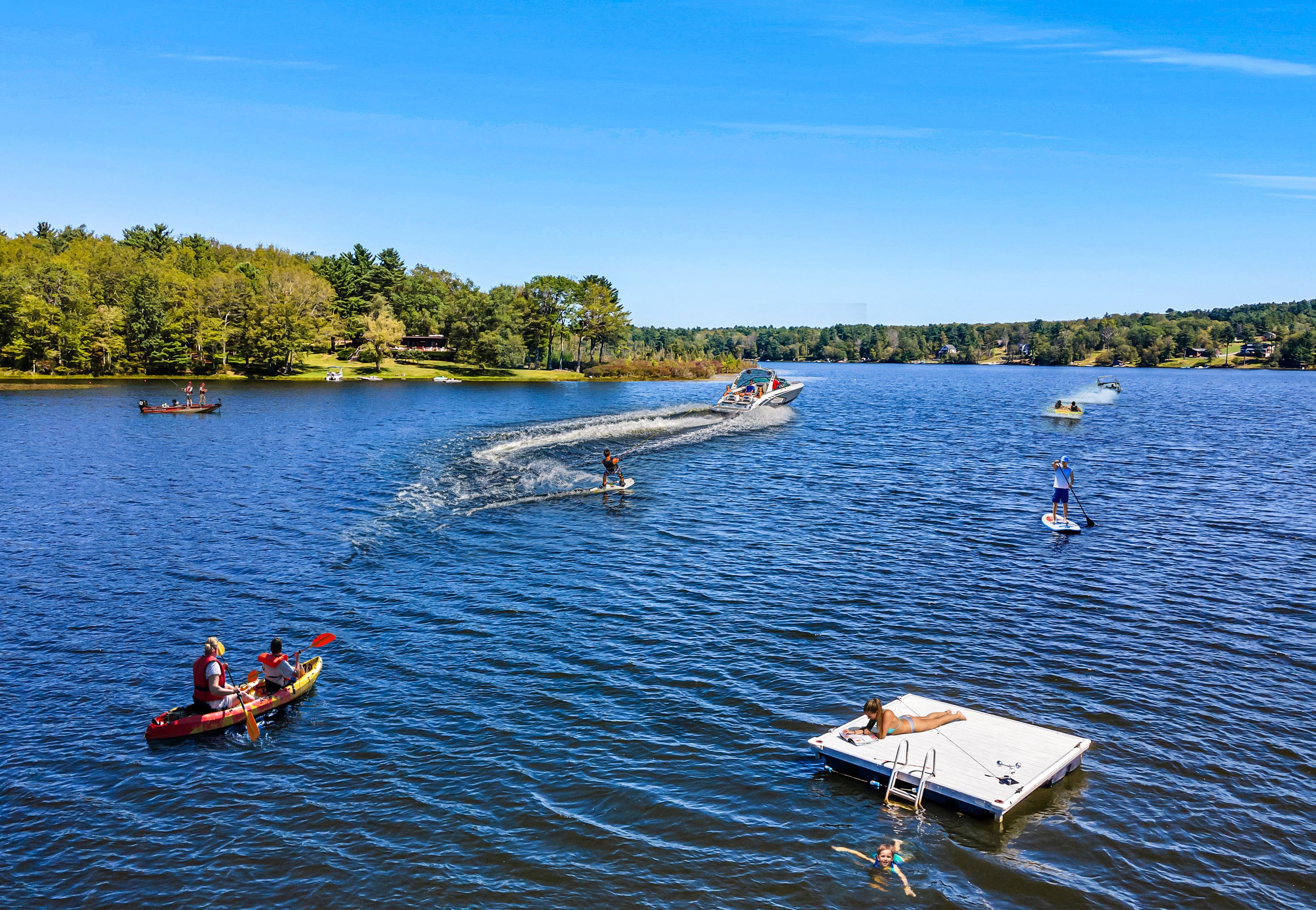 A lake with boats and paddleboards, surrounded by trees and houses.