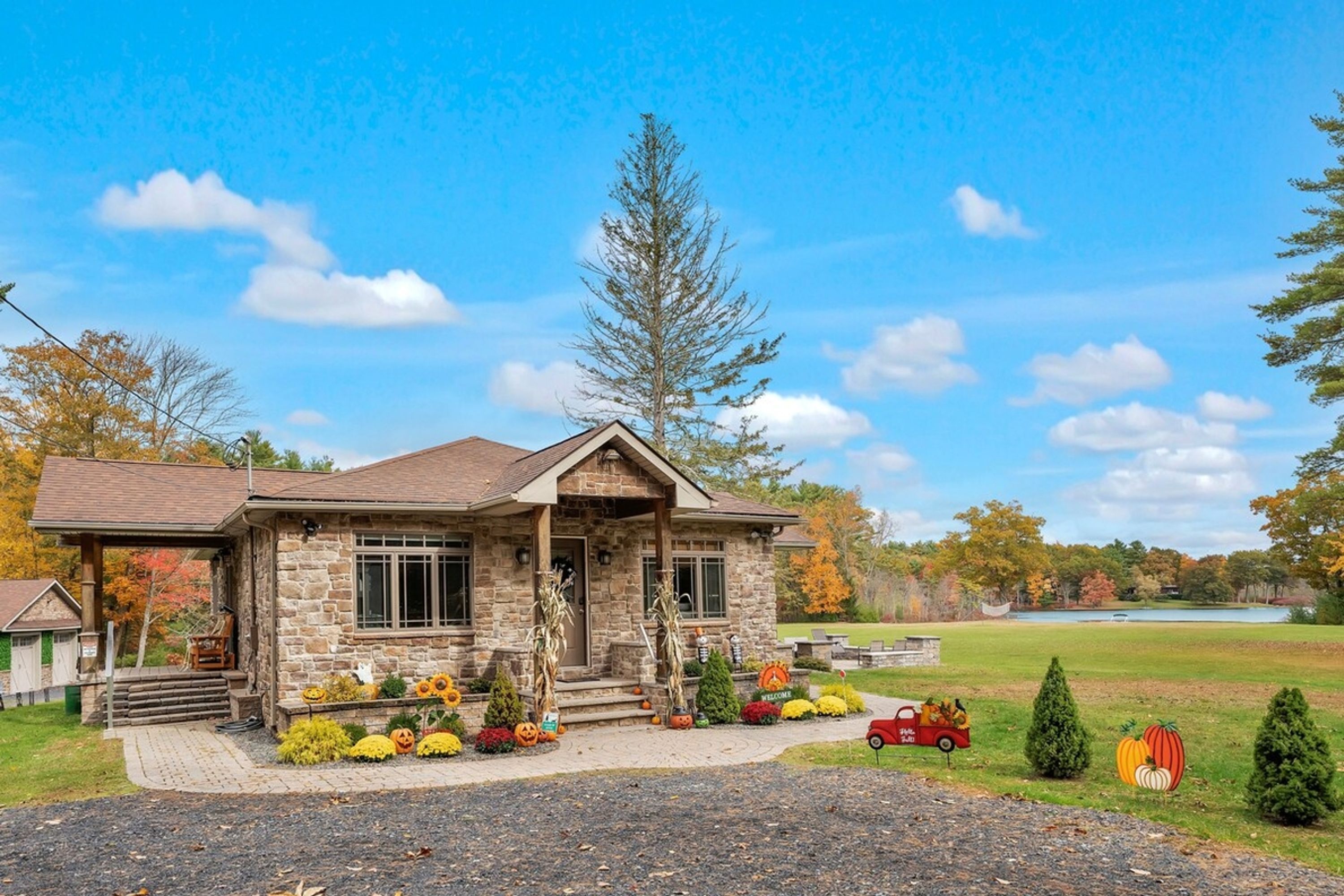 A stone house with a porch, surrounded by autumn foliage and a lake view.