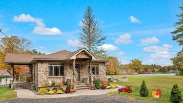 A stone house with a porch, surrounded by autumn foliage and a lake view.