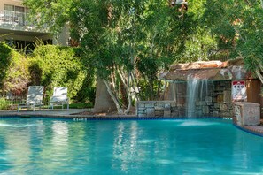 A swimming pool with a waterfall feature, surrounded by lush greenery and a stone wall. - Desert Oasis @ Las Palmas - Amazing view (St. George)