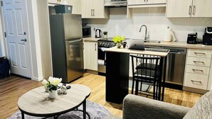 A compact kitchen with a refrigerator, microwave, stove, and sink. There is a small dining area with a table and two chairs.
