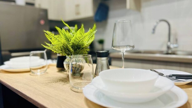 A neatly arranged dining table with white plates, a glass of water, a salt shaker, and a small potted plant.