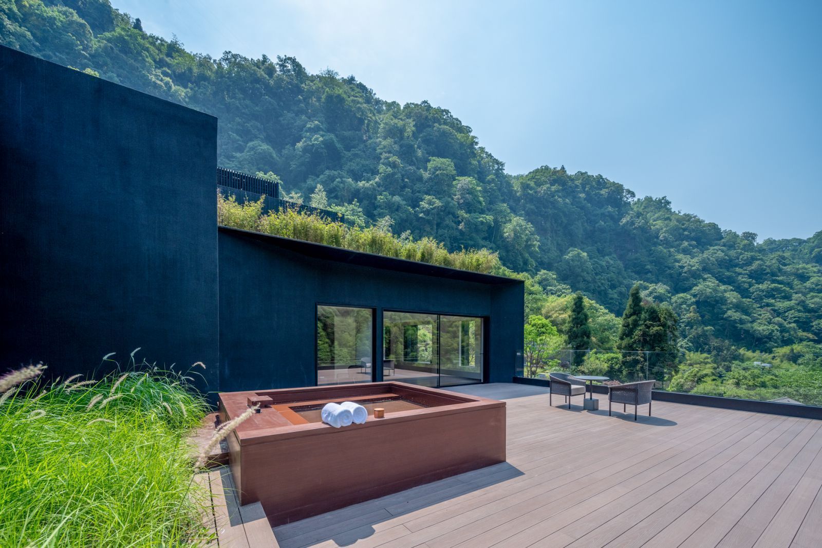 Um edifício moderno com uma varanda grande, uma banheira de hidromassagem e vista para uma encosta arborizada.
