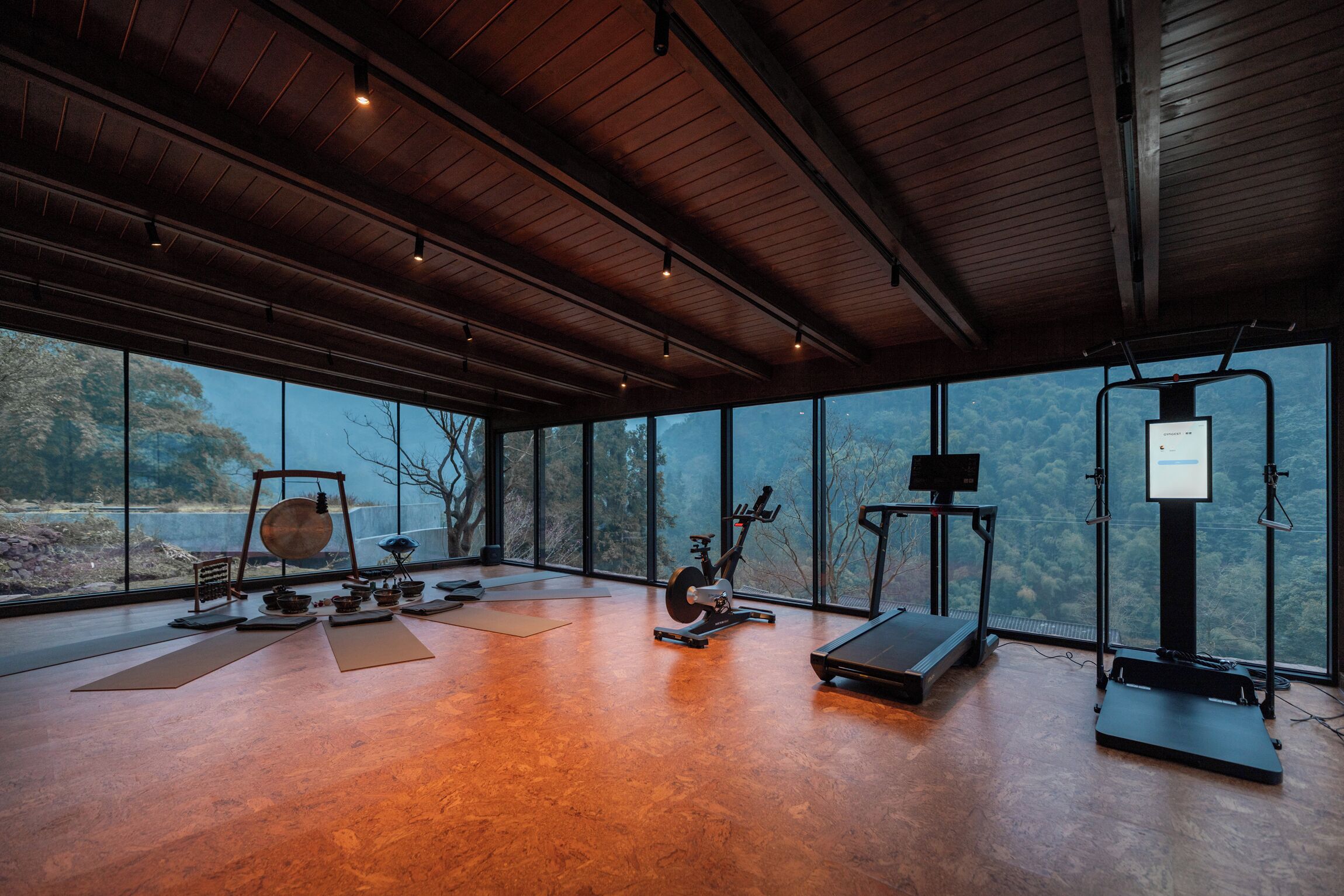Un gimnasio espacioso con equipo de ejercicio, ventanas amplias y techo de madera.