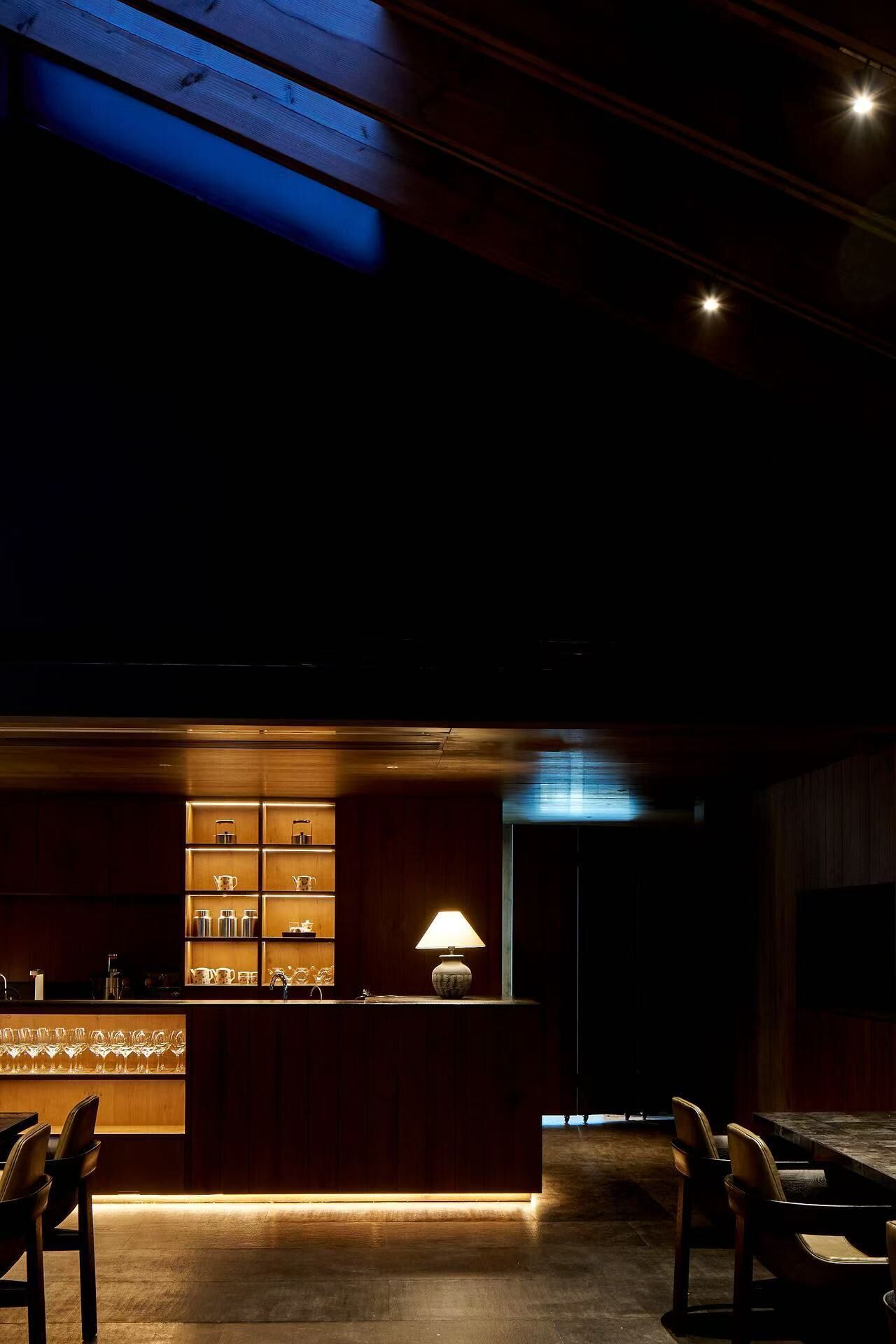 A dimly lit bar area with wooden furnishings and a central table with a lamp.