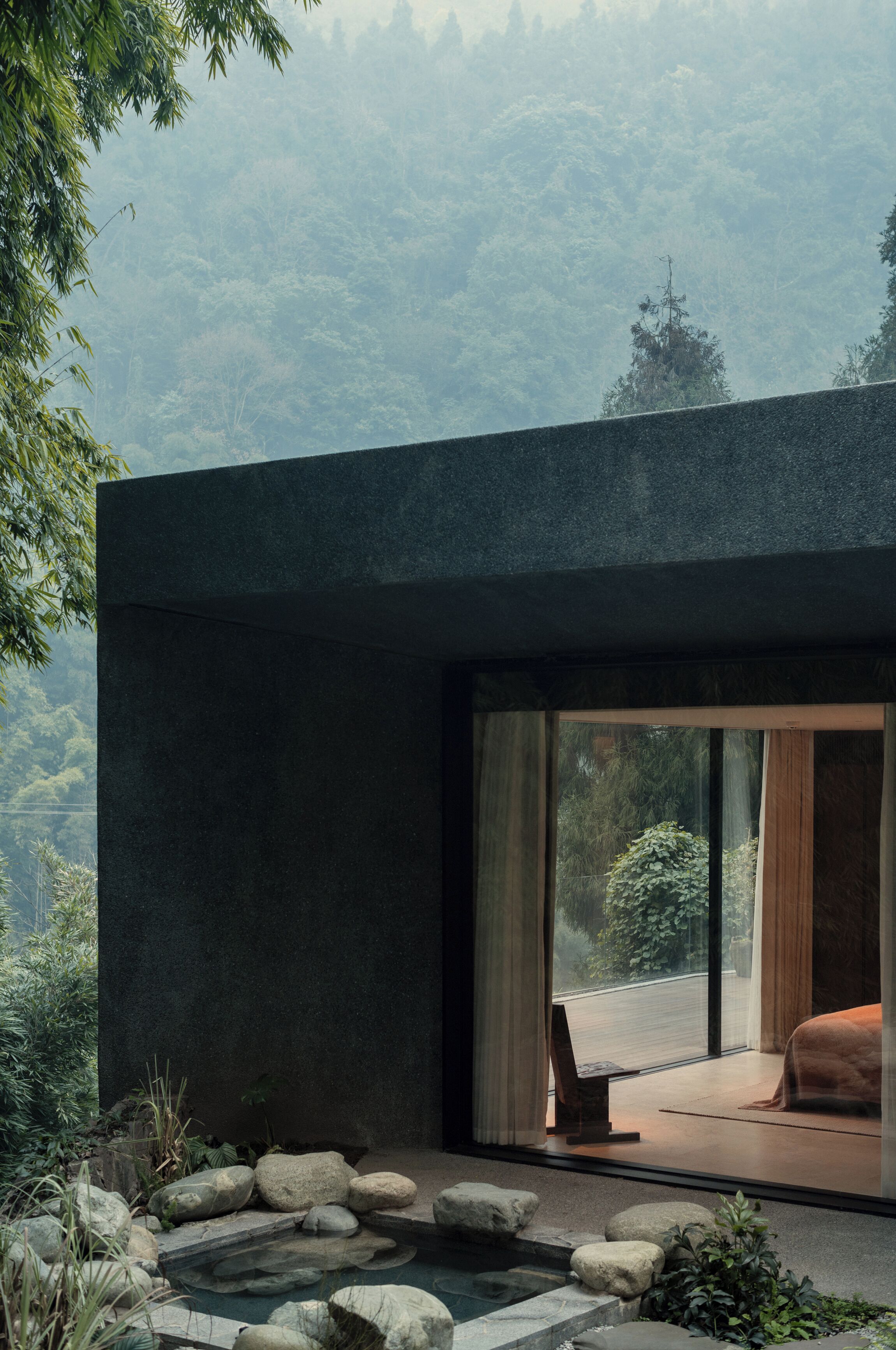 A modern interior with a stone pathway leading to a seating area, large windows offering a view of a forested landscape.