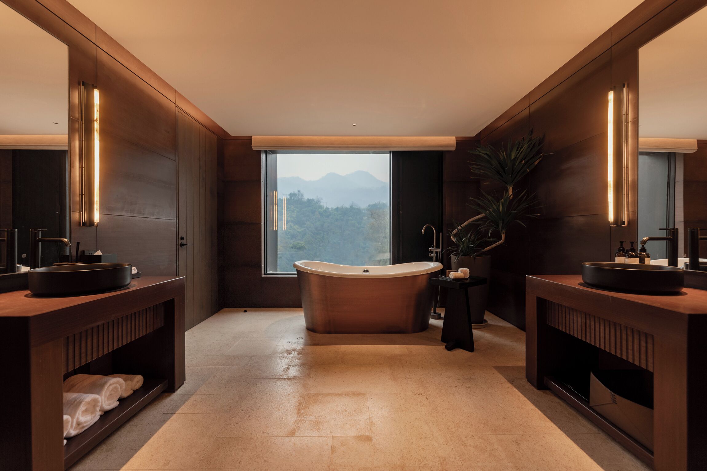 A modern bathroom with a freestanding bathtub, two sinks, and a large window offering a mountain view.