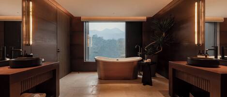 A modern bathroom with a freestanding bathtub, two sinks, and a large window offering a mountain view.