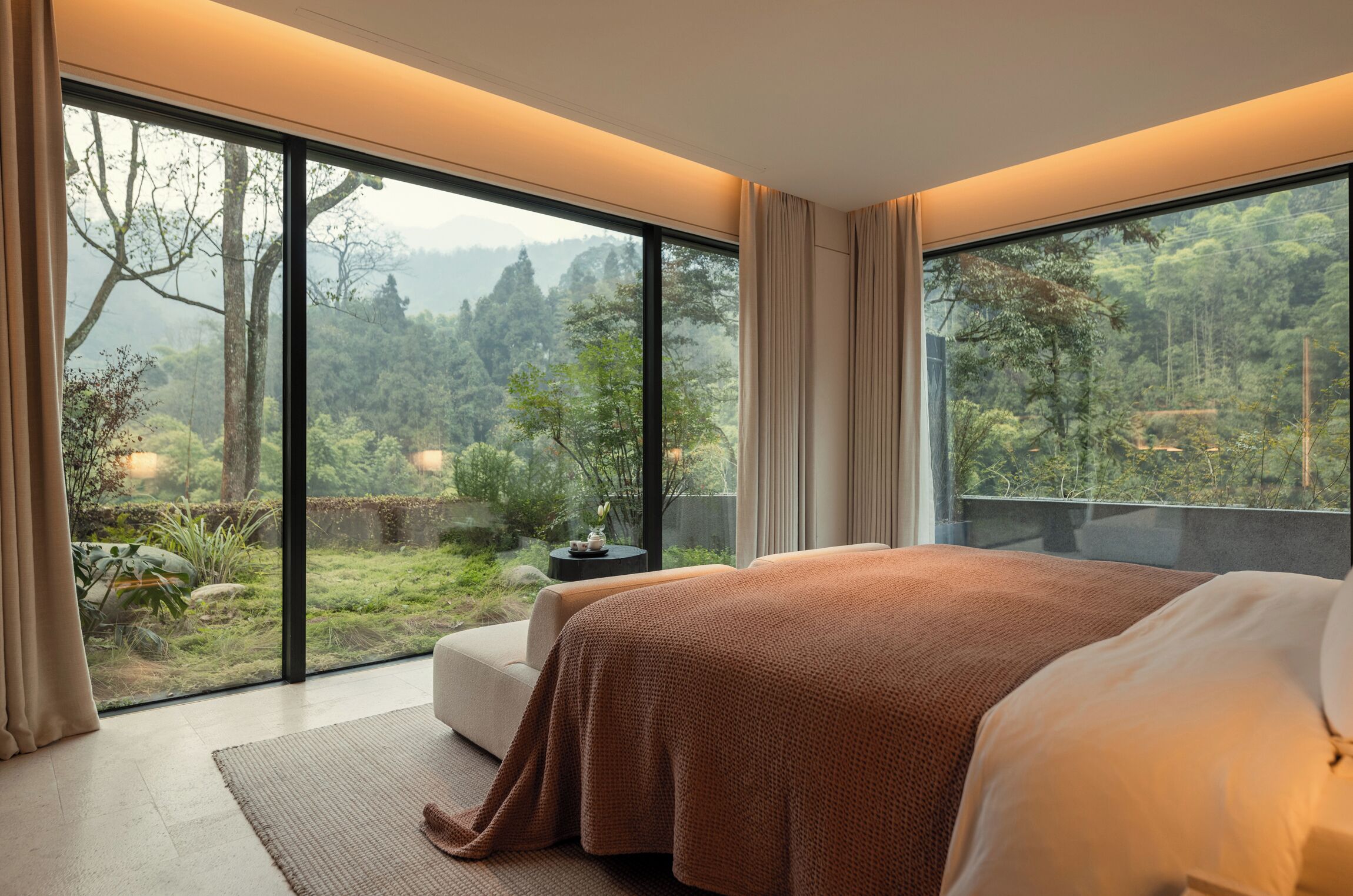 Une chambre dotée d’un grand lit, donnant sur un jardin luxuriant, et possédant une porte-fenêtre coulissante.
