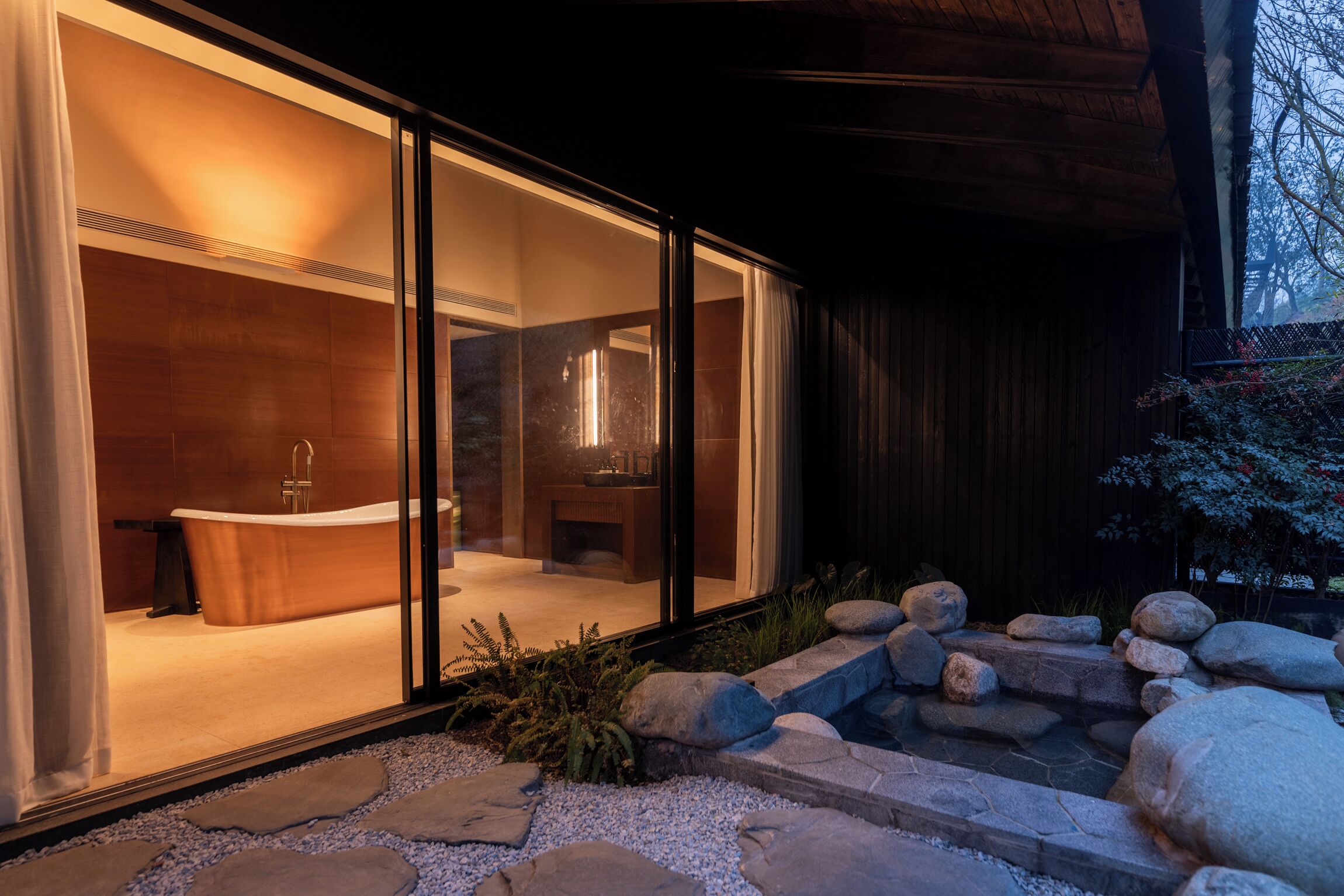 A modern spa with a large bathtub, a wooden interior, and a stone pathway leading to the entrance.