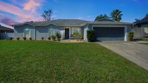 A single-story house with a garage, a front lawn, and a driveway. - Spacious 3BR Home, Gym, Pool Table, Central Location (Deltona)
