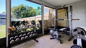 A home gym with various exercise equipment including dumbbells, a bench, and a squat rack. - Spacious 3BR Home, Gym, Pool Table, Central Location (Deltona)