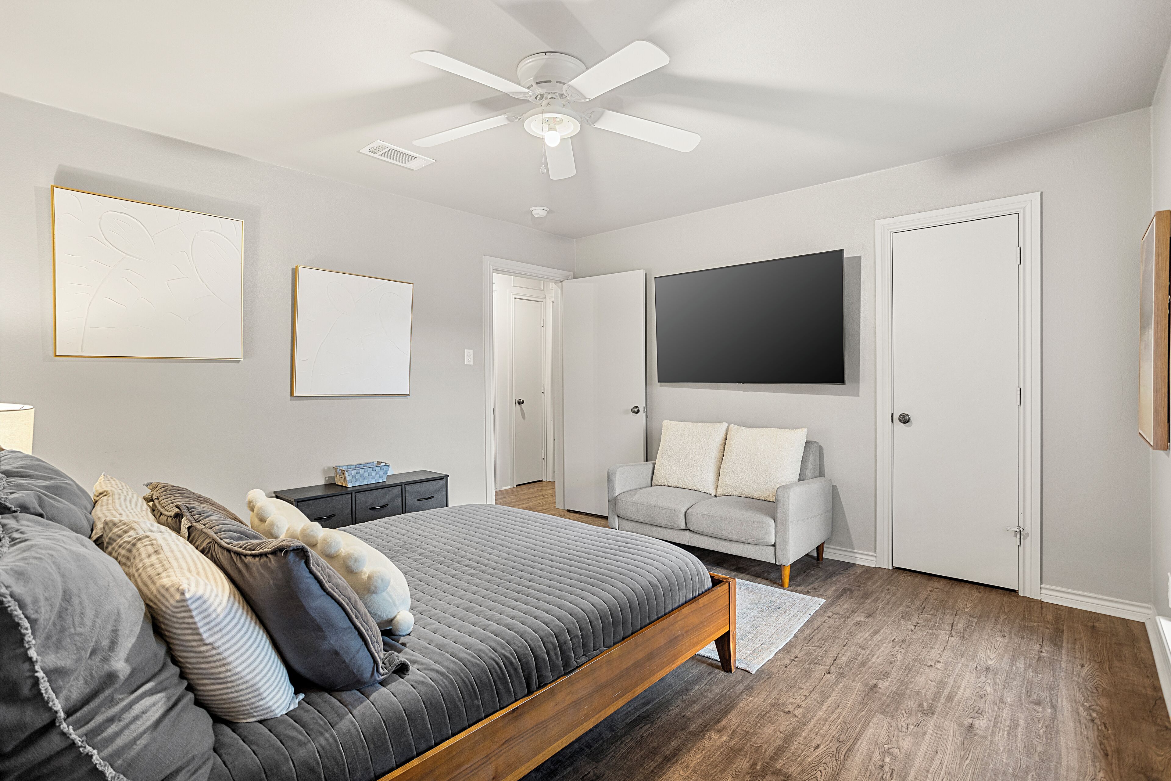 A bedroom with a bed, a gray sofa, a TV, and a ceiling fan.