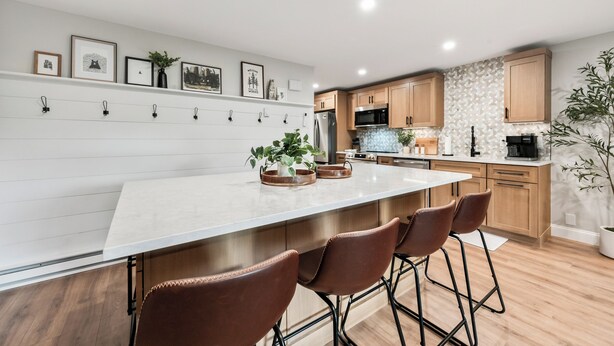 A modern kitchen with a large island, wooden cabinets, and a white backsplash.