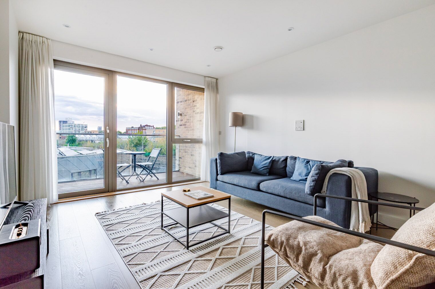 Una sala de estar moderna con un sofá azul, una mesita de centro y vistas a la ciudad a través de amplios ventanales.