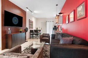 Ein modernes Wohnzimmer mit roter Akzentwand, einem an einer Holzvertäfelung montierten Flachbildfernseher, einem Glastisch und einem dunkelgrauen Sofa.