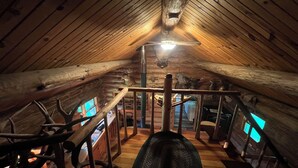 Habitación en ático con vigas de madera, techo inclinado, escalera de madera y una lámpara en el techo.