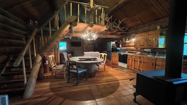 Interior rústico de una cabaña con comedor, cocina y chimenea.