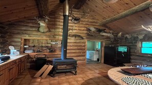 Een rustiek cabinteinterieur met een houtkachel, houten kastjes, een keukenhoek en opgehangen dierenkoppen aan de muren.