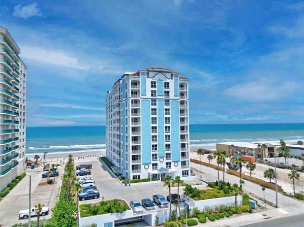 Een meerlaags hotel met een centrale binnenplaats, parkeerplaats en uitzicht op het strand.