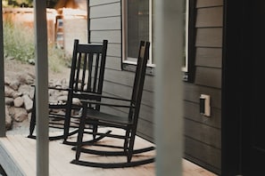 Ein Schaukelstuhl auf einer Holzterrasse vor einem Haus mit Fenster und Tür.
