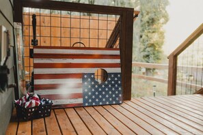 Una terraza de madera con un portón rústico que presenta un diseño de la bandera estadounidense, un pequeño ventanal circular y una cesta con objetos a la izquierda.