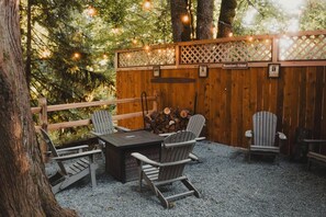 Ein Sitzbereich im Freien mit Adirondack-Stühlen und einem Tisch, umgeben von einem Holzzaun und Lichterketten.