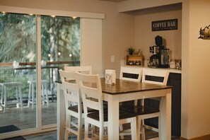 Un'area ristorazione con tavolo e sedie, un angolo caffè con insegna e vista attraverso una porta in vetro.