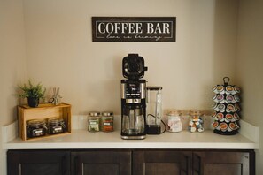 A kitchen counter with a coffee maker, jars of spices, and a coffee mug rack.