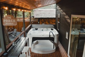 Et område med jacuzzi, en træterrasse og et skilt med teksten "The Porch Sit & Relax", samt en glasdør ind til et andet rum.