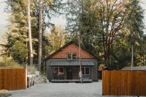 Eine zweistöckige Holzhütte mit dunklem Dach und einer Veranda mit zwei Stühlen.