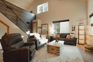 Ein geräumiges Wohnzimmer mit hoher Decke, einer Treppe und großen Fenstern, die natürliches Licht hereinlassen.