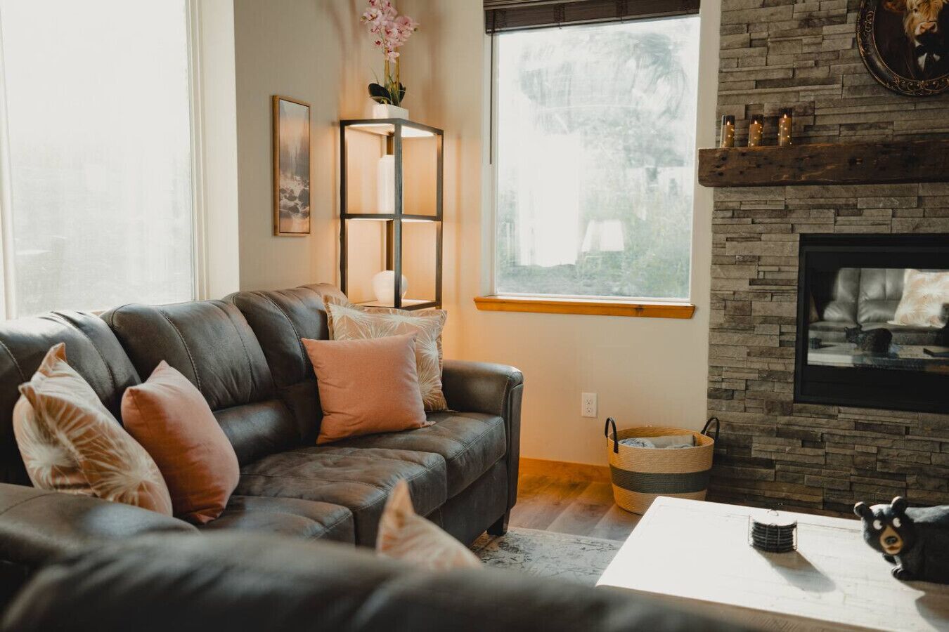 A living room with a black leather sofa, a fireplace, a window with a view, and a decorative wall shelf.