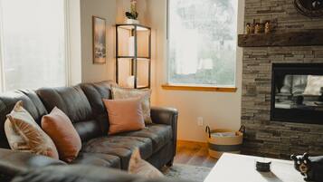 A living room with a black leather sofa, a fireplace, a window with a view, and a decorative wall shelf.