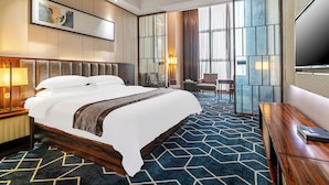 A hotel room with a large bed, a desk, a chair, a TV, and a large window with curtains.