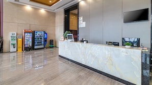 A hotel reception area with a marble counter, a flat-screen TV, vending machines, and a clean, modern design.