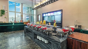 A buffet setup with multiple serving stations, a large window with a city view, and a modern chandelier.
