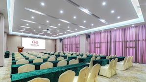 A conference room with rows of tables and chairs, a projector screen, and a logo on the wall.
