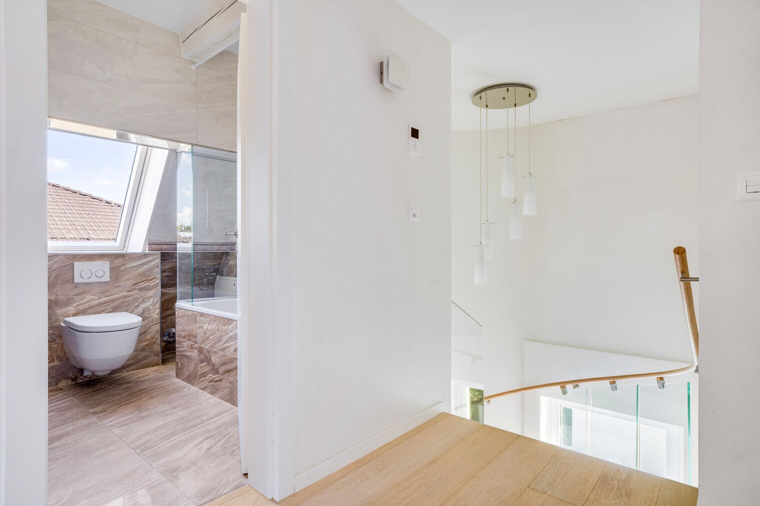 A modern bathroom with a toilet, marble flooring, and a glass shower enclosure.