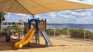 A playground with a slide and climbing structures, located near a waterfront with a bridge in the background. - Tumby Bay Caravan Park (Tumby Bay)